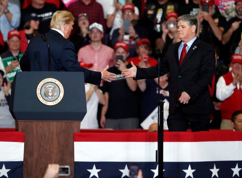 Two men go to shake hands on state at a large event.