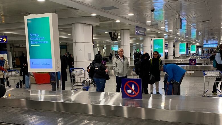 Sustainable Saskatchewan billboards can be seen in 10 airports in Canada. These travellers in Montreal wait for their bags next to a series of digital ads.