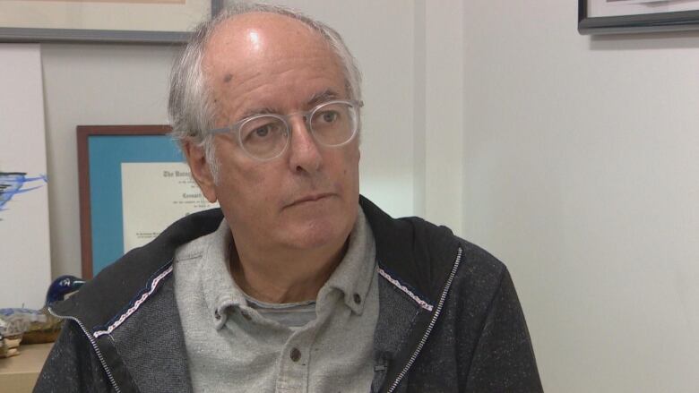 A bald spectacled man sits.