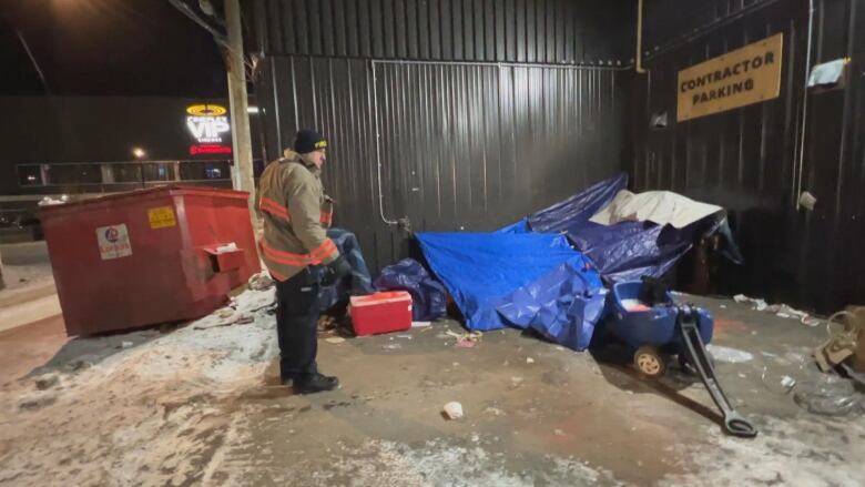 An encampment made of blue sheets in a parking lot corner.