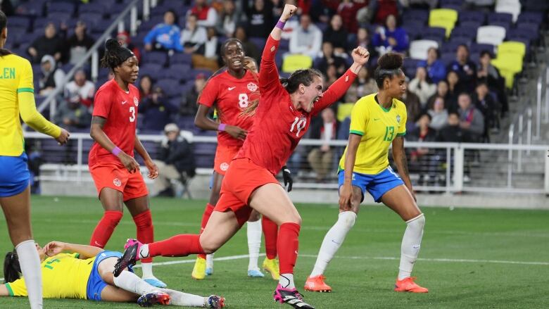 A female soccer player raises here arms while yelling in celebration.