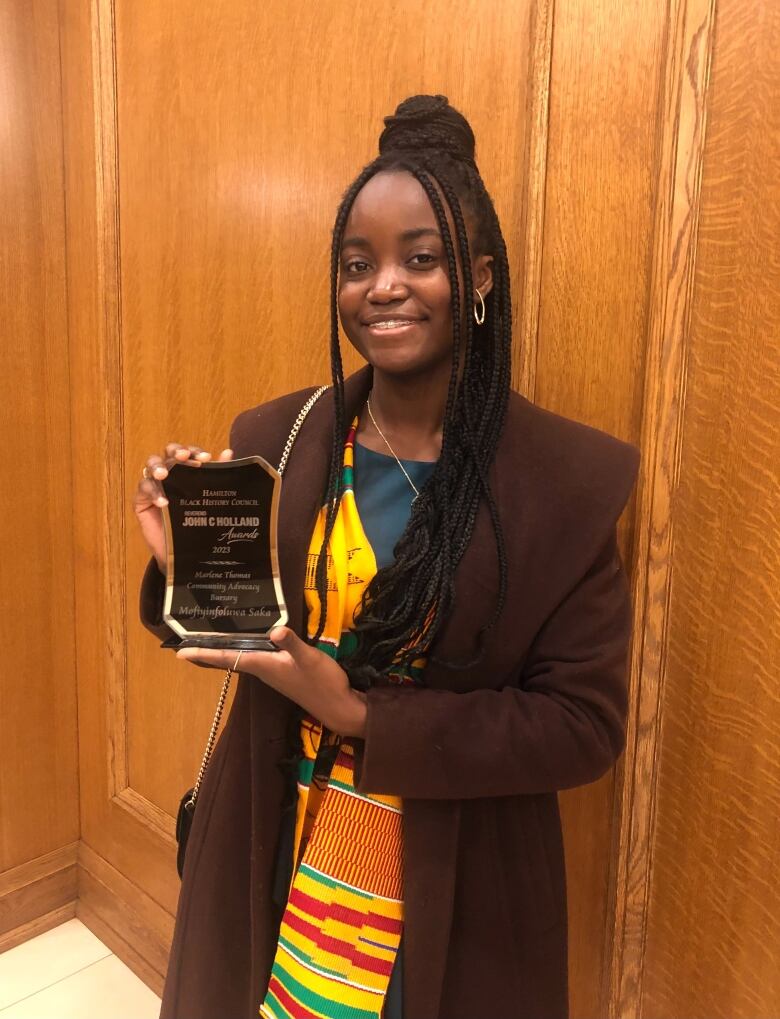 A girl holding an awards that reads: Hamilton Black History Council, Reverend John C. Holland Awards, 2023. Marlene Thomas Community Advocacy Bursary, Mofiyinfoluwa Saka.