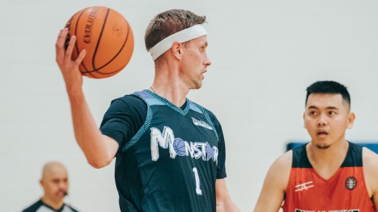 A man holding a basketball in his right hand is being challenged by a defender in a basketball game.