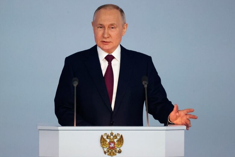 A man in a suit is shown speaking at a podium with an insignia on it.