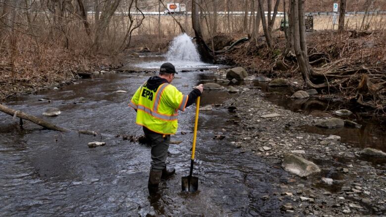 A man with a shovel walks in a stream.