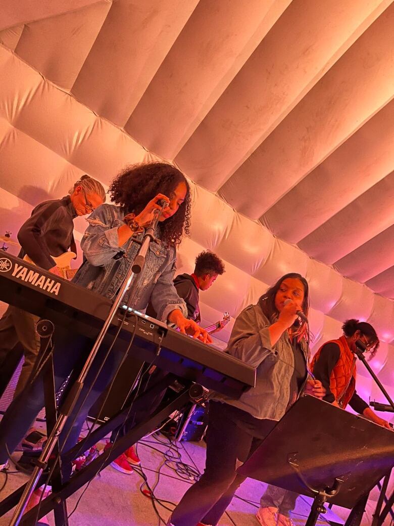 Five members of The Yaadies band perform on stage under a white tent.