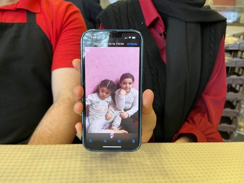 A girl holds up a phone showing a picture of two girls sitting down. 