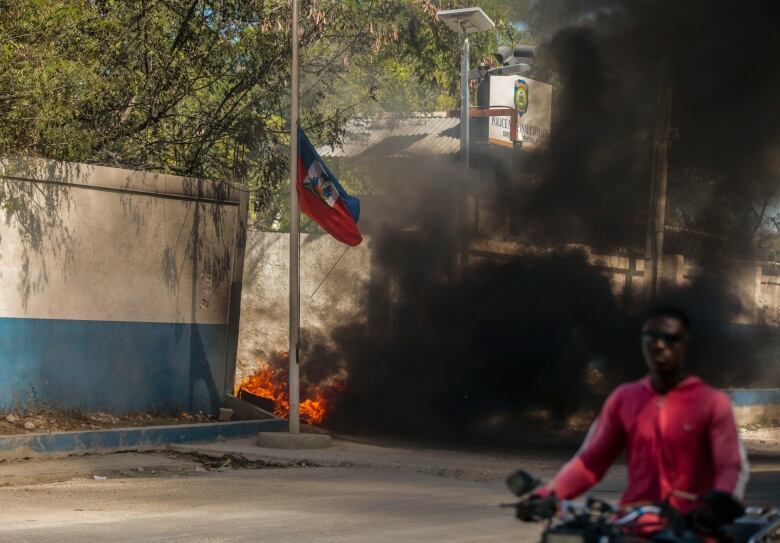 A taxi driver drives past a burning tire set outside the door of police headquarters by officers as they protest bad police governance in Port-au-Prince, Haiti, on Jan. 26. 