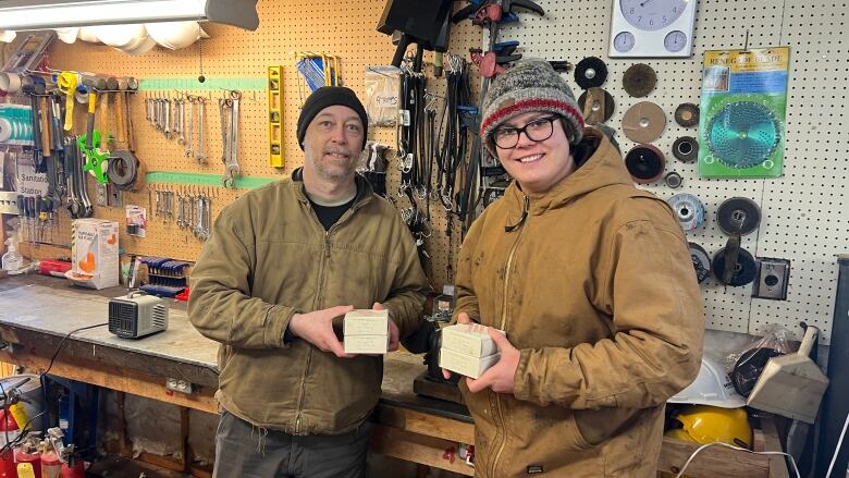 A man and boy stand in a shop, holding two small boxes each.