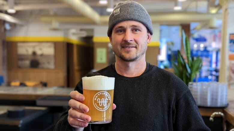 A man wearing a grey toque holds a glass of beer