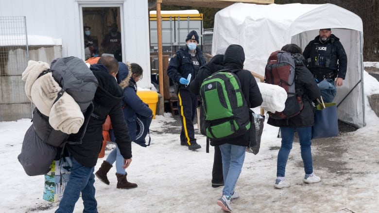 People in jackets walk towards police officers in the winter.