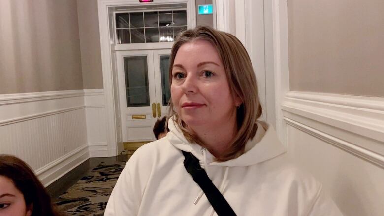 A blonde woman in a white sweater stands in a dim hallway of city hall in Halifax