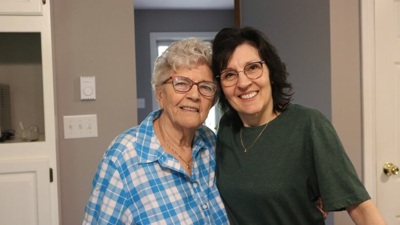 An elderly woman and a younger woman smile at the camera