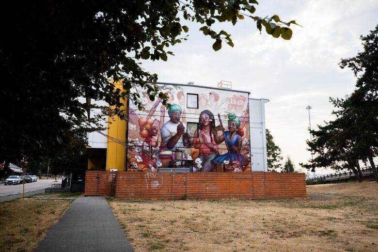 A building in a grass field is shown with a mural celebrating Black history is painted on the side. 