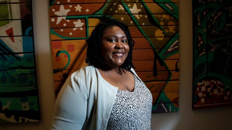 A Black woman is pictured in front of an artwork.