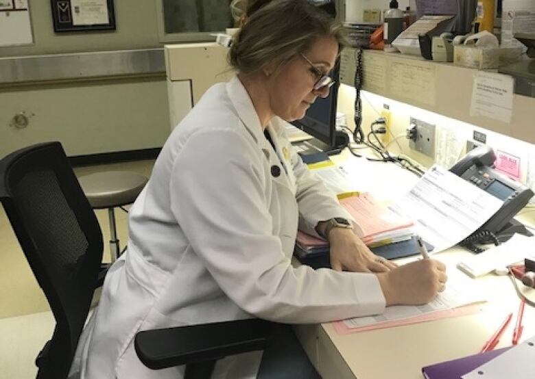 Kirsten Luomala sits at a desk in a medical facility and writes in a patient's file.