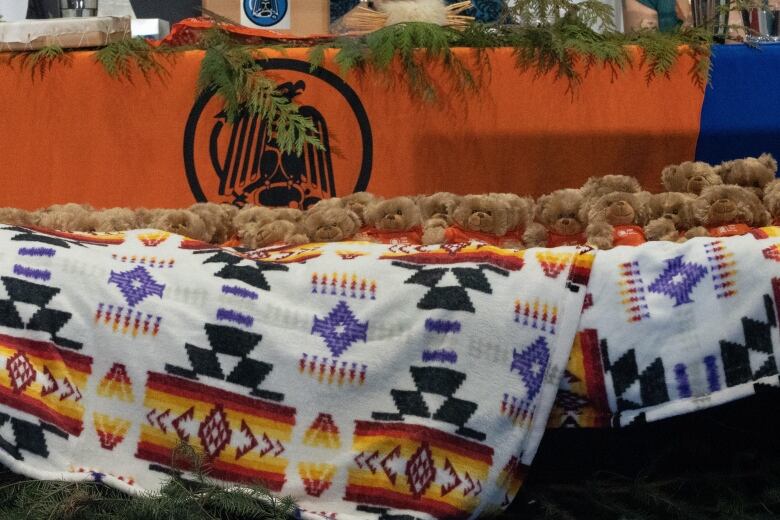 Dozens of teddy bears with orange shirts lie on a blanket. 