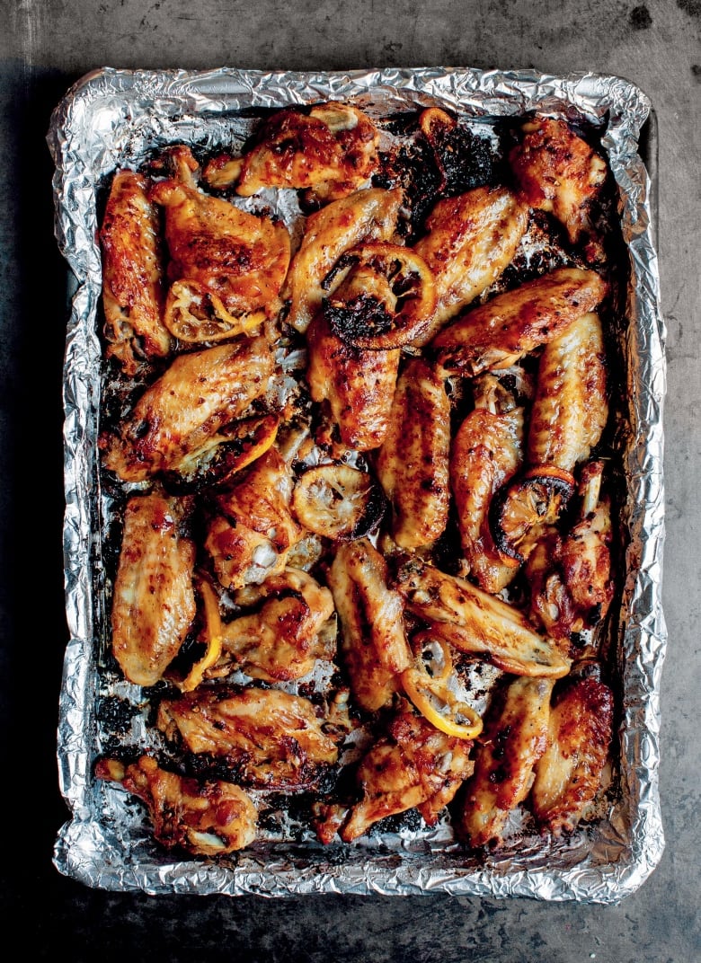 Roasted chicken wings and lemon slices on a baking sheet covered in tin foil, sitting on a grey surface. 