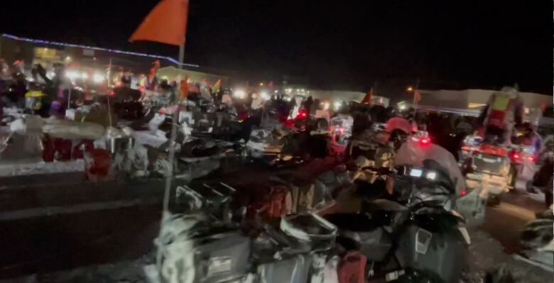 A jumble of snowmobiles left to idle as riders are welcomed by community on a cold winter night.