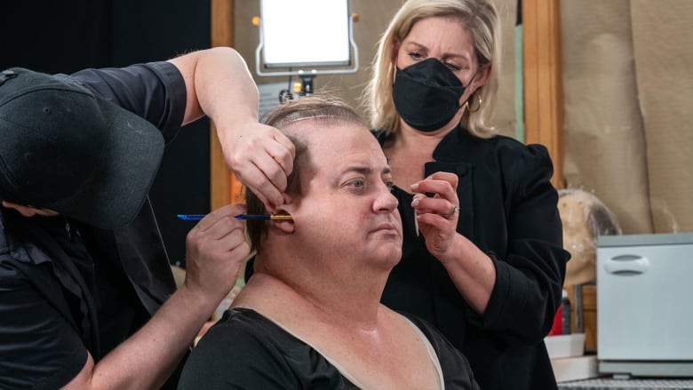 Adrien Morot adds a bit of glue to Brendan Fraser's face while Annemarie Bradley styles his hair.