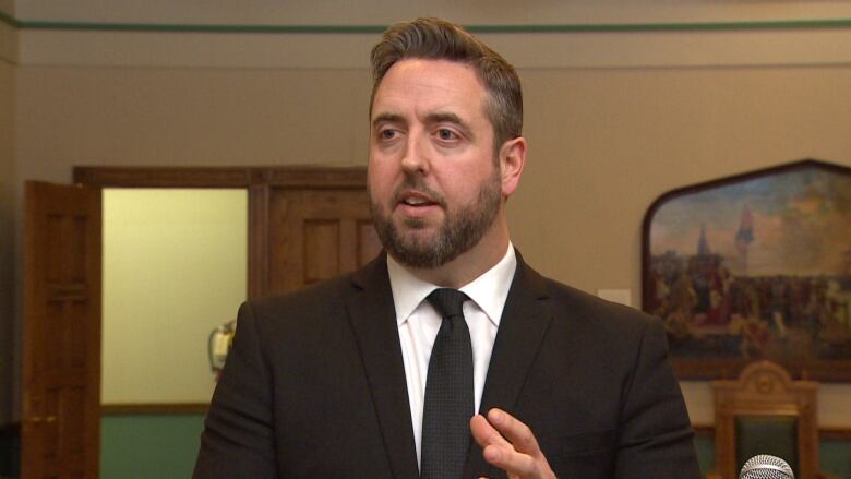 A man wearing a black suit talks to reporters.