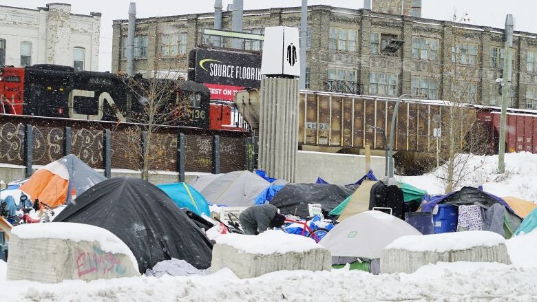 Tents are covered in snow, a CN train is in the background