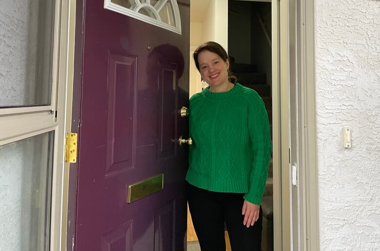 A smiling woman opens the door to her home.