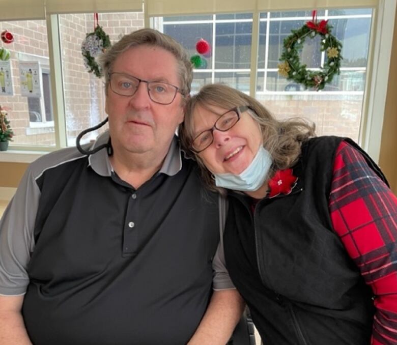 An older man, on the left, and woman, on the right, smile. The woman rests her head on the man's shoulder.