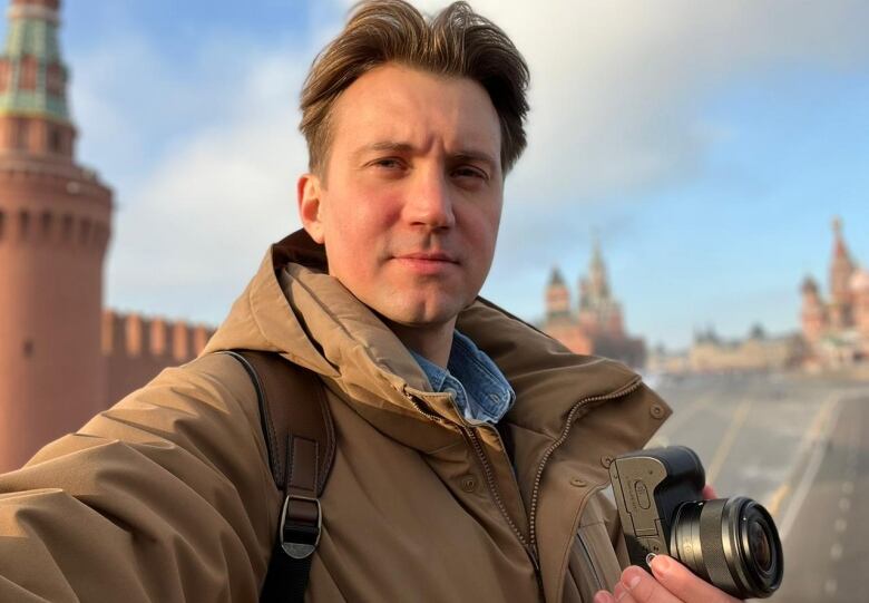 A man wearing a light-brown winter jacket holds a camera.