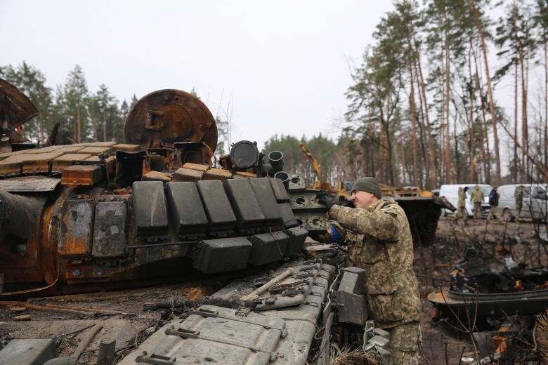 A man dressed in camouflage works on taking parts from a tank that has been destroyed  