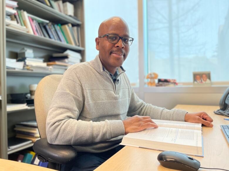 A Black man, Carlton-James Osakwe, is shown in his office at Mount Royal University in Calgary, where he is a professor of business.