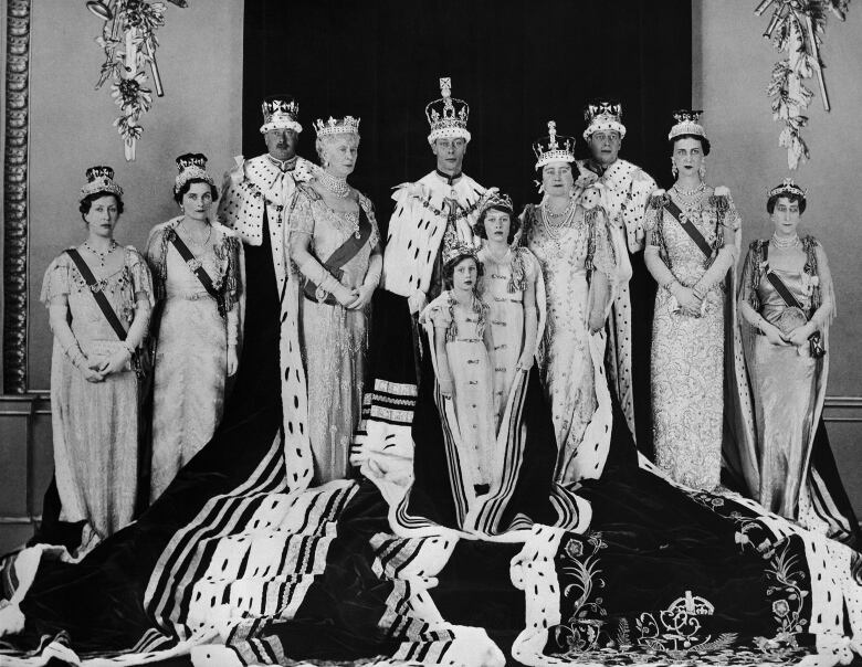 Several people stand posed for a formal portrait, with some wearing elaborate robes and crowns.