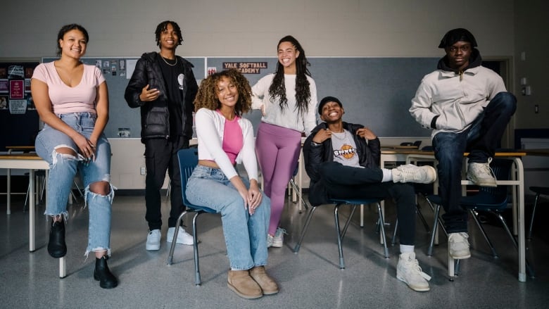 A group of Black students pose by the classroom desks smiling. 