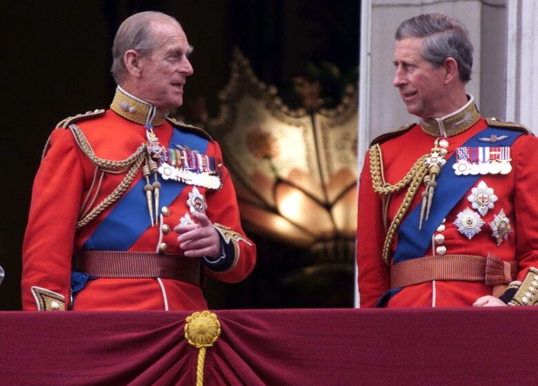 Two people stand on a balcony in front of open doors.