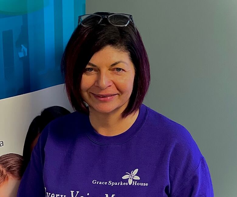 A woman wearing a purple sweater smiles into the camera.