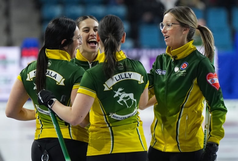 Four female curlers gather in a circle while smiling in celebration on the ice.