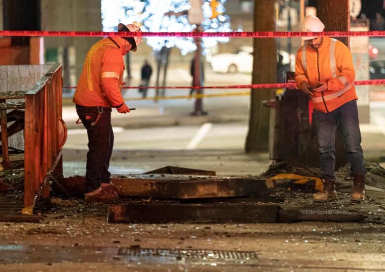 Two workers look into an underground vault.