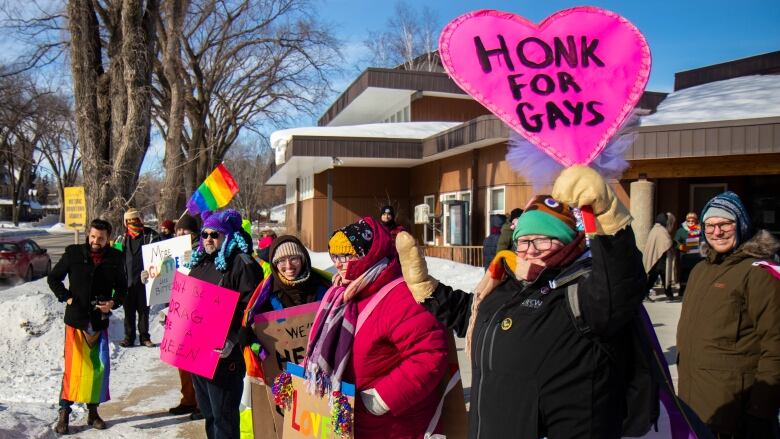 Ralliers dressed in winter gear hold pro LGBTQ signs.