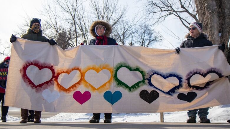 Ralliers dressed in winter gear hold pro LGBTQ signs.