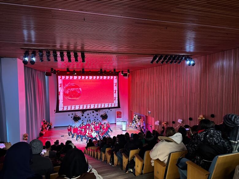 This photo shows a room of people sitting in a levelled hall with seating rows.