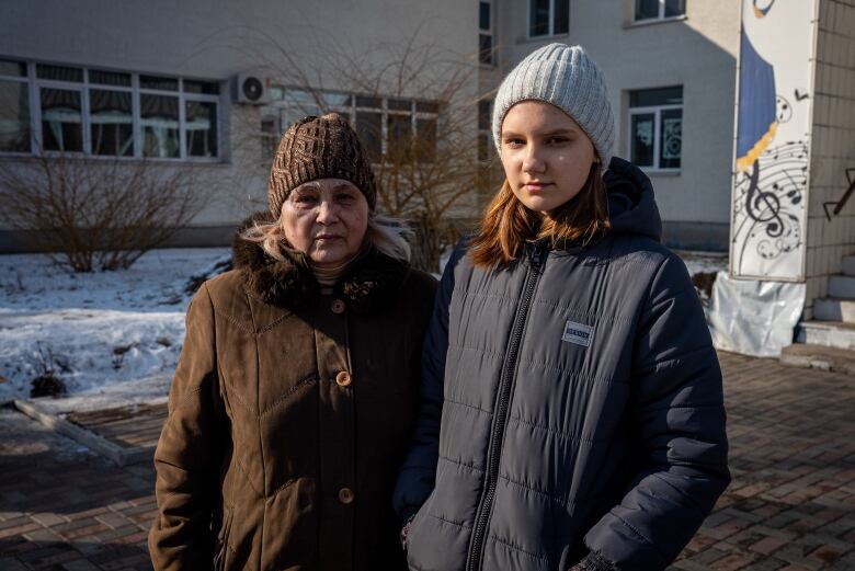 A grandmother stands beside her granddaughter in front of a building.