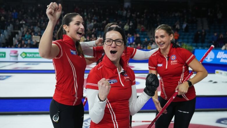 Four female curlers smile and wrap their arms around each other in celebration on the ice.