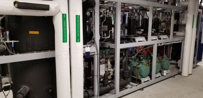 A large black tank full of CO2 is nestled among black and white pipes and valves. Some green compressors can be seen to the right.