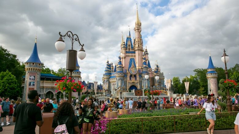 People walk in front of a castle-like structure at a theme park. 