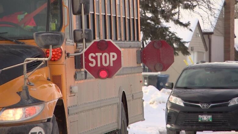 A closeup of the front of a yellow school bus parked on a snow-covered street with a red 