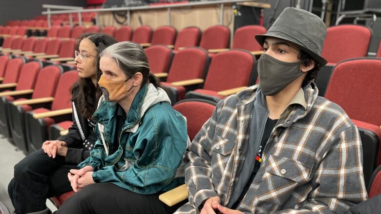 Three people sit on chairs in a school theatre.