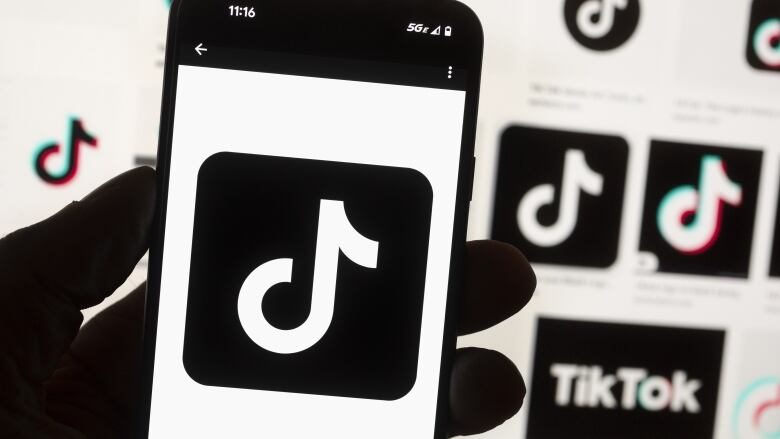 A hand holds a cell phone displaying the TikTok logo.