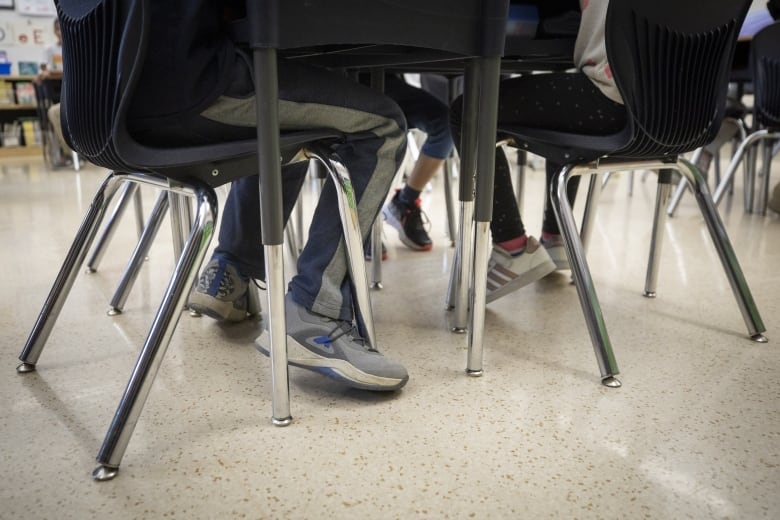 The feet of students under a table in a classroom are shown.