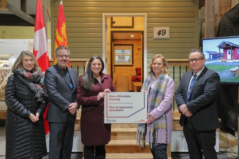 Five people standing in front of a tiny home. The two women in the middle are holding a sign that says 