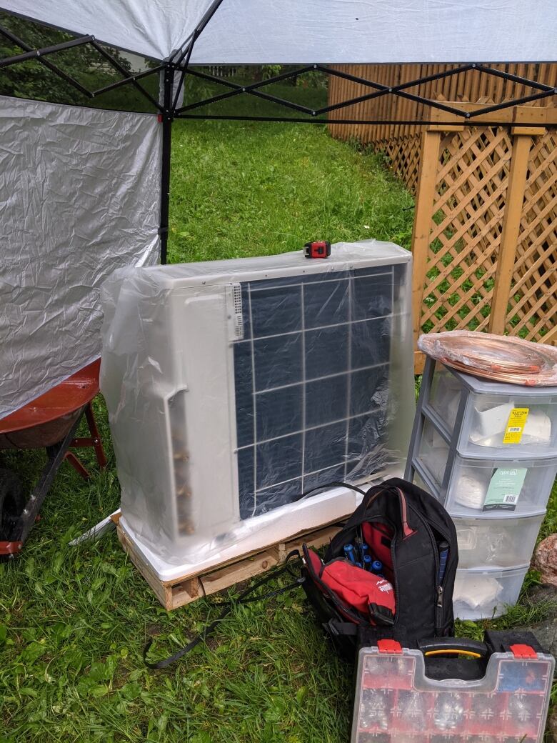 A heat pump in a yard with a backpack next to it.